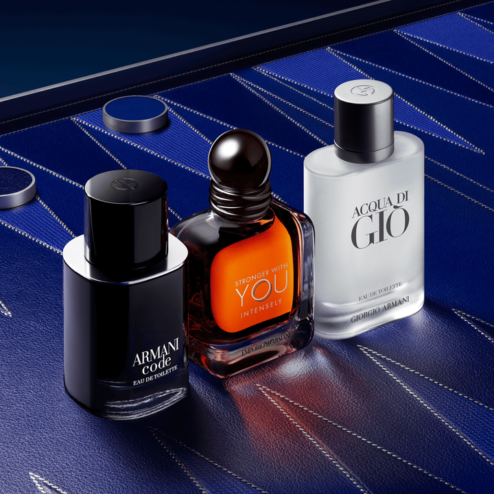 Een verfijnd trio van mannelijke Armani-iconen: Armani Code, Stronger With You Powerfully en Acqua di Gio. De flacons staan op een diepblauw lederen achtergrond met couture geometrische patronen, de belichaming van mannelijke elegantie.