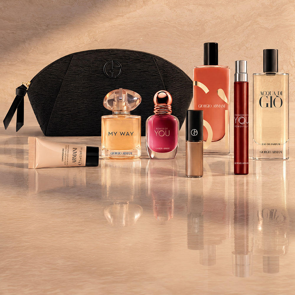 Een zwarte Armani Beauty-toilettas met parfums, make-up en huidverzorgingsproducten tegen een beige achtergrond.