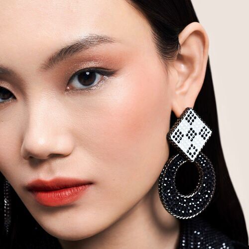 Model met een verfijnde make-up en opvallende, grote oorbellen in zwart en wit.