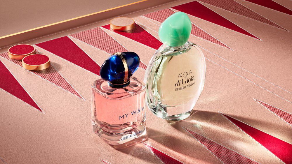 Armani My Way Eau de Parfum bottle and Acqua di gioia Eau de parfum bottles on a pink and red geometric backgammon board background.