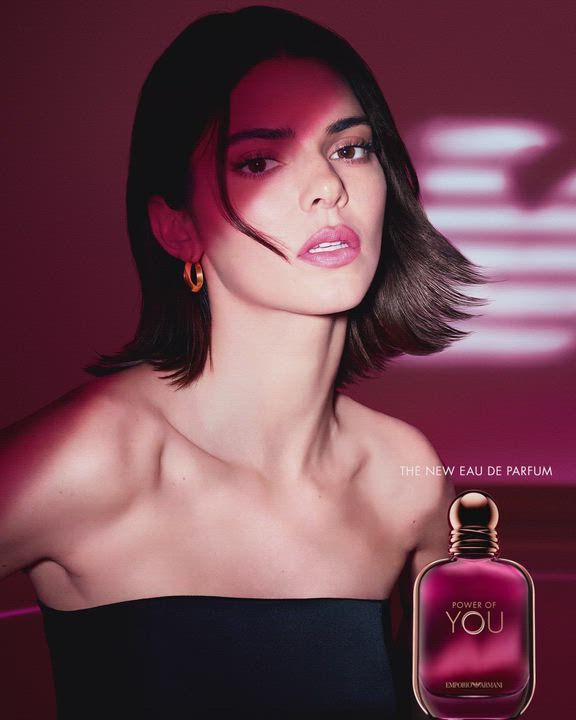 Une publicite pour l'Eau de Parfum « Power of You » d'Emporio Armani. L'image presente le mannequin Kendall Jenner sur la gauche, regardant vers l'appareil avec une expression douce. Elle a les cheveux courts et noirs, porte un haut bustier noir et des boucles d'oreilles creoles dorees. A droite, un flacon de parfum d'un rose violace profond est expose avec les inscriptions « Power of You » et « Emporio Armani ». En arriere-plan, le logo de l'aigle Armani stylise et lumineux se detache sur un fond magenta fonce. Le texte indique « POWER OF YOU » en haut a droite et « THE NEW EAU DE PARFUM » en bas a droite.