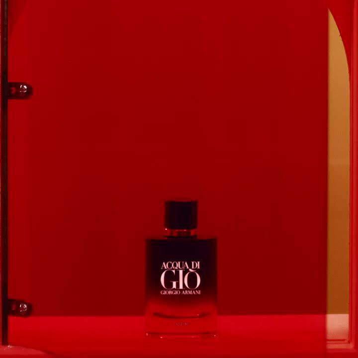 A bottle of Acqua di Gio by Giorgio Armani displayed on a bright red background, partially enclosed by a transparent red structure.