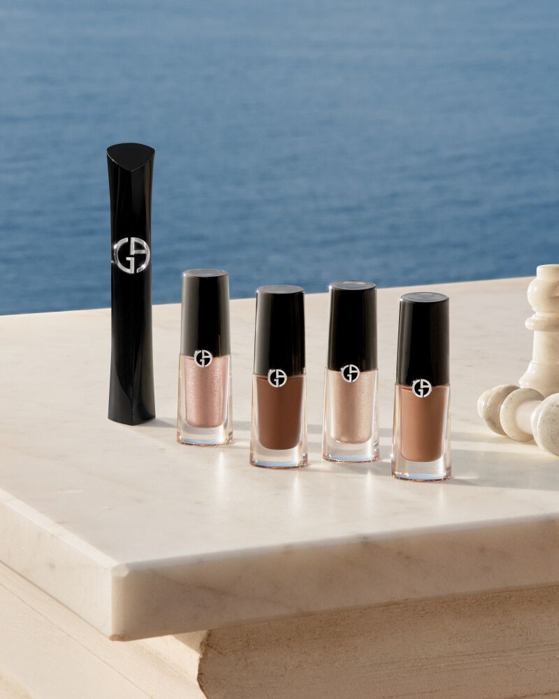 Eye make-up products arranged on a terrace table, with the sea behind.