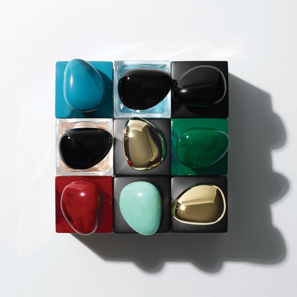 A top-down view of a grid containing nine smooth, teardrop-shaped objects in various colors, including teal, black, green, red, gold, and a light mint shade. The objects are placed on contrasting black and clear square bases, creating a visually striking pattern.