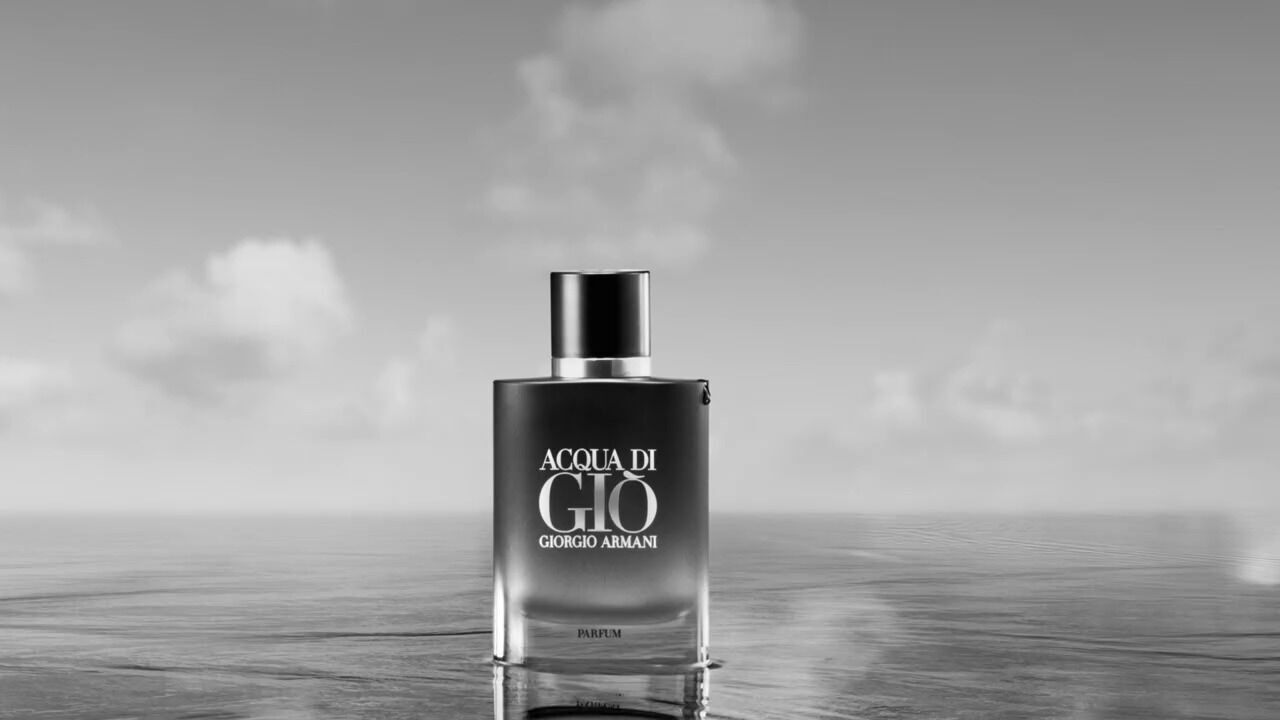 A black and white image of a Giorgio Armani Acqua di Gio perfume bottle, set against a serene, cloudy water backdrop.