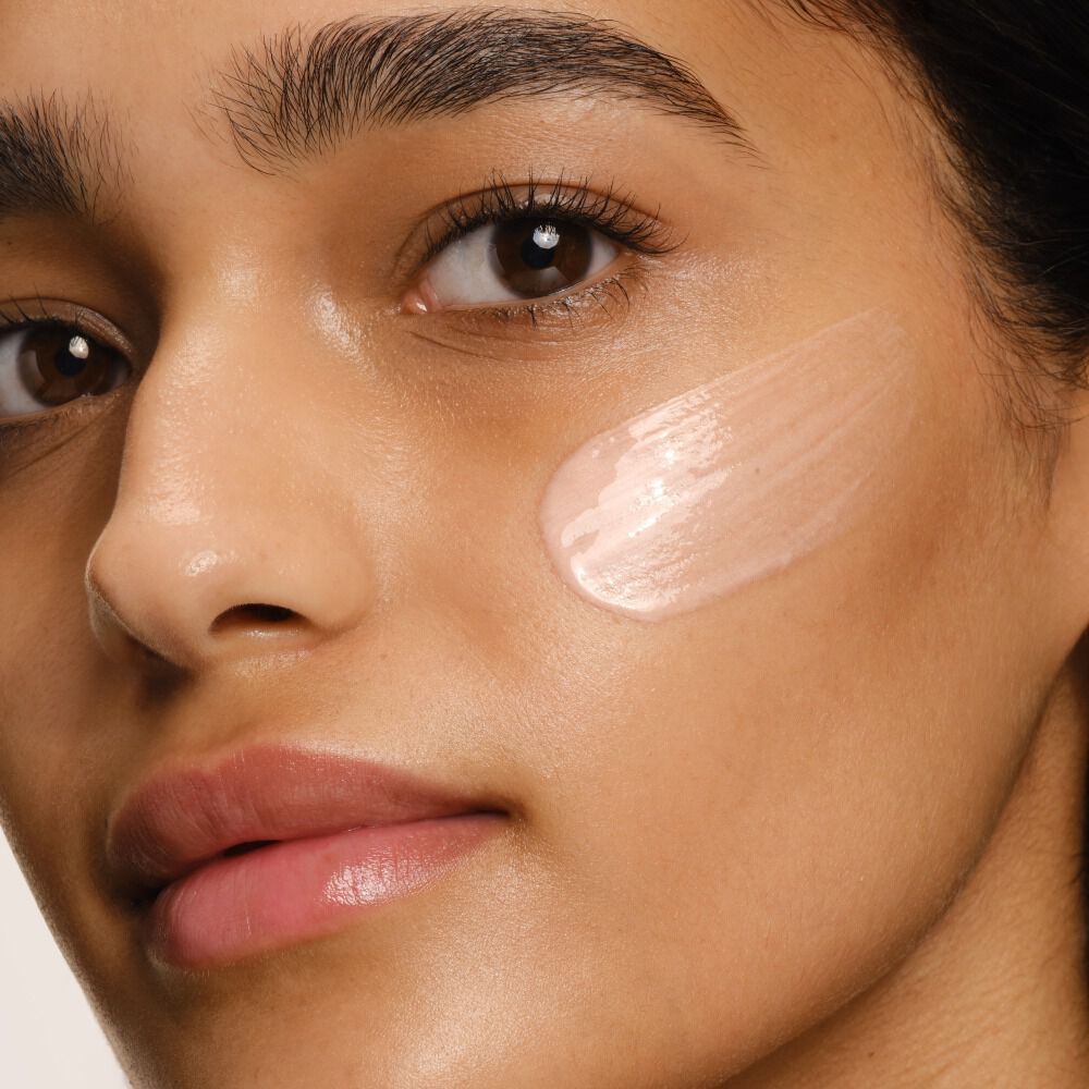 A close-up of a person's face with a luminous, light pink swatch of the Luminous Silk Illuminating Primer applied to their cheek.