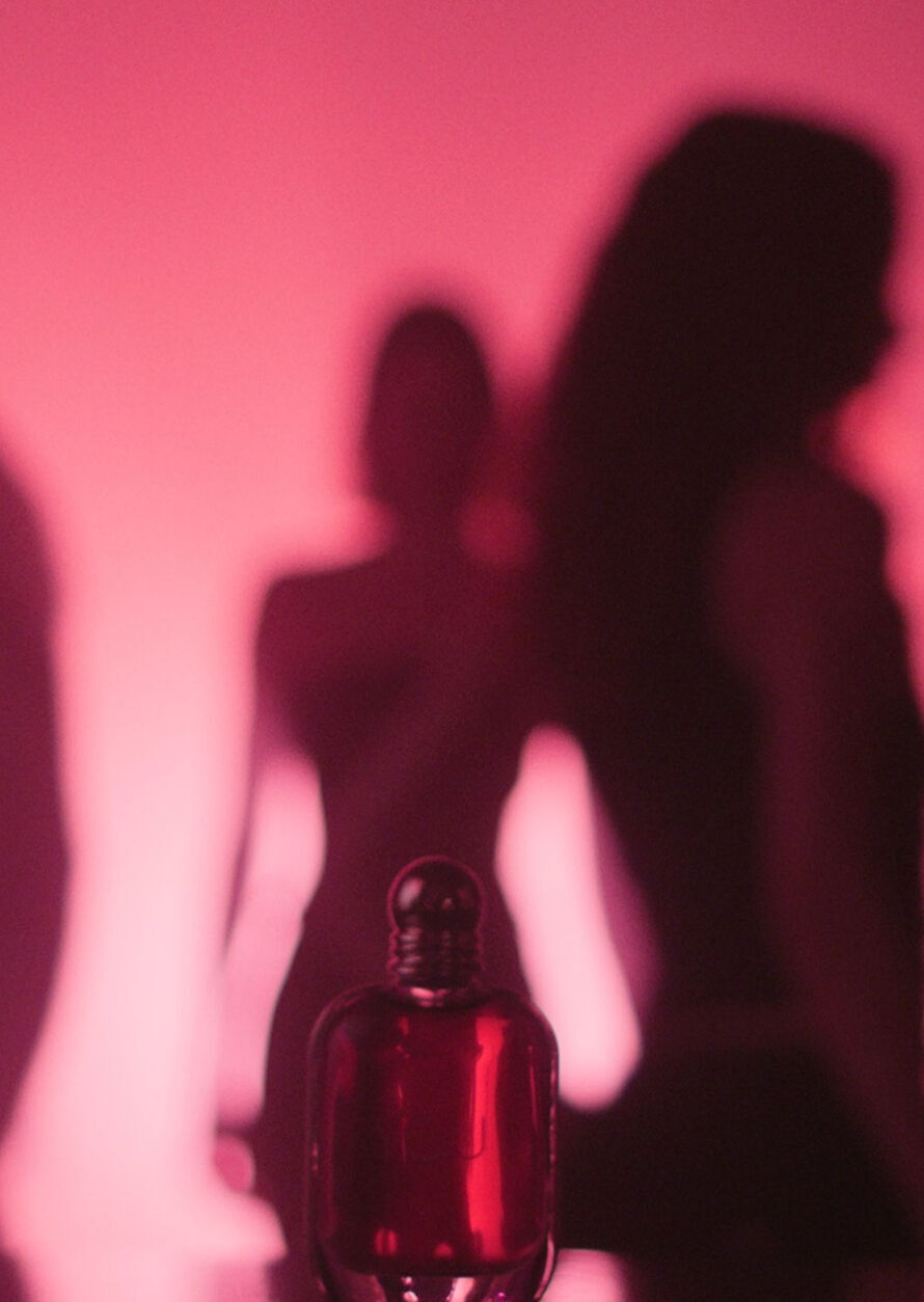 Une publicite artistique et feutree pour « Power of You » d'Emporio Armani. Au premier plan, le flacon de parfum de couleur rubis est visible mais partiellement ombrage. Derriere lui, la silhouette sombre d'une femme, probablement Kendall Jenner, est centree sur un fond rose et magenta doux et lumineux. D'autres silhouettes floues apparaissent sur les cotes, creant une impression de profondeur et de mystere. Un bouton de lecture et une fleche de navigation sont visibles, indiquant qu'il s'agit d'un extrait de video ou d'une galerie numerique.