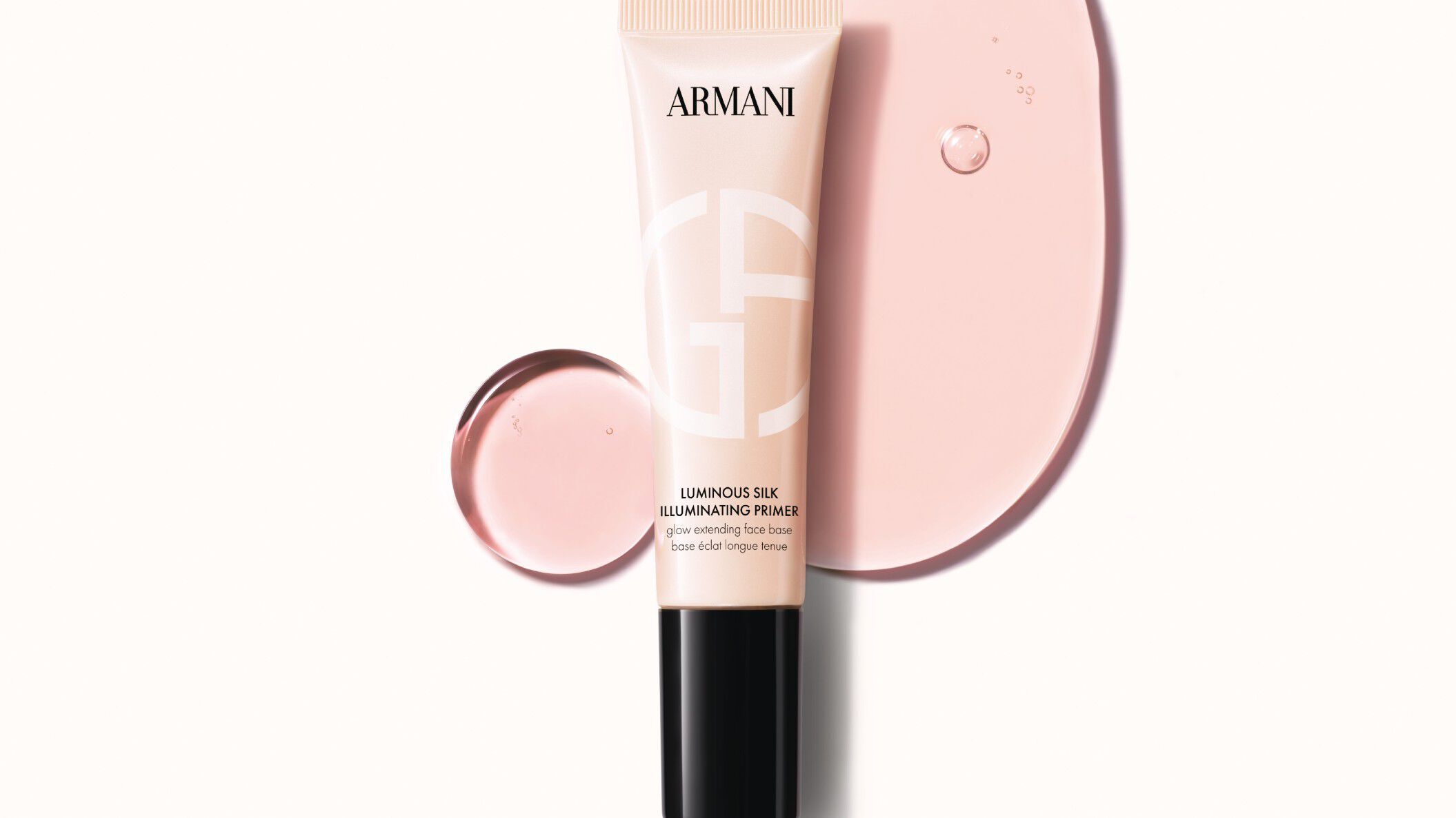 A visual of ARMANI Luminous Silk Illuminating Primer, pale pink tube with GA logo and black pump on a peach background with creamy swirls.