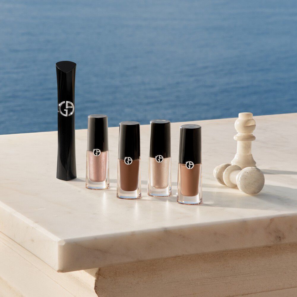 Armani beauty eye essentials resting on refined white marble against a deep Mediterranean sea. Featuring the signature mascara and luminous, earthy shades of Eye Tint liquid eyeshadow for a sophisticated and effortless look.