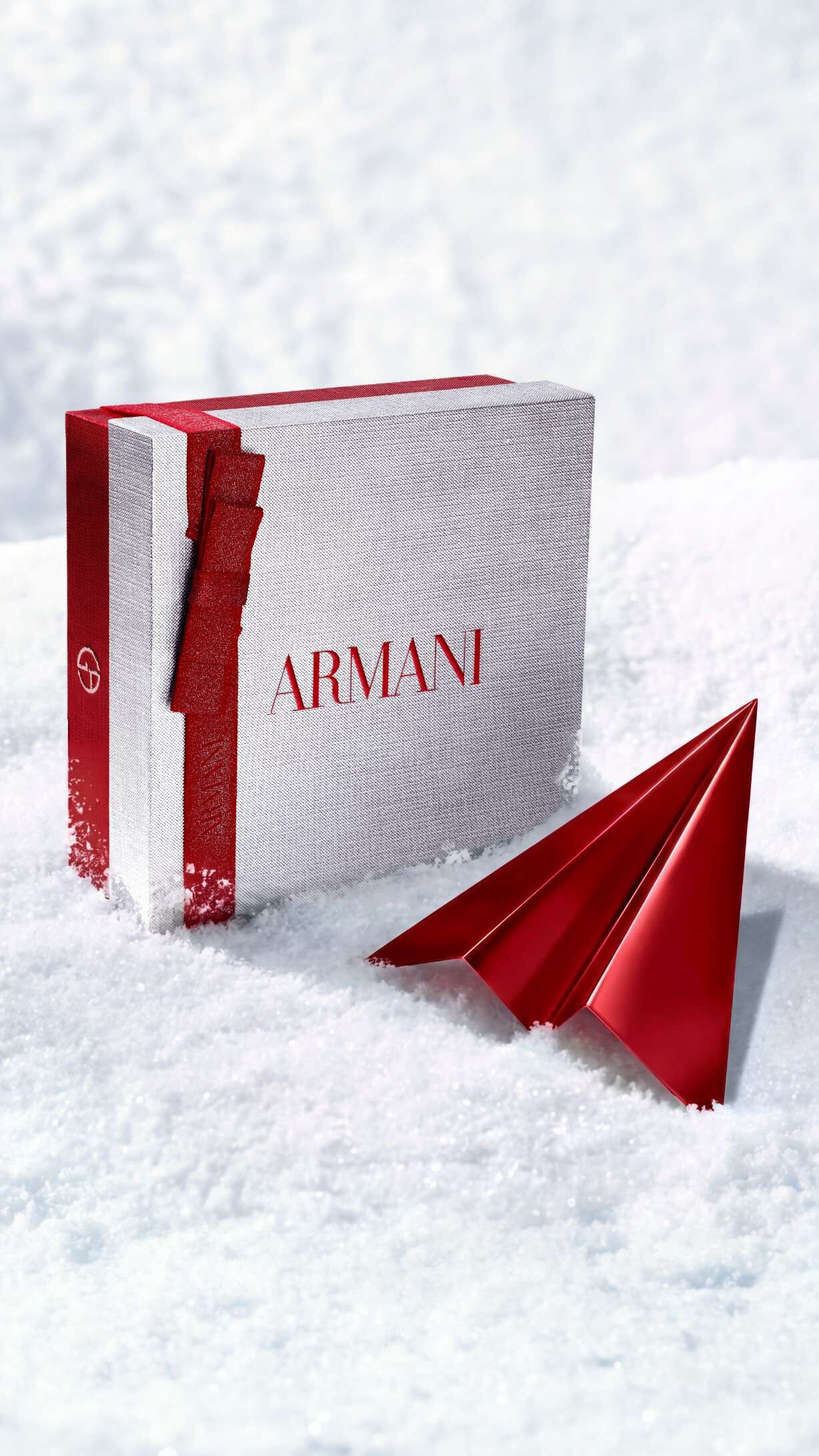 Zilverkleurige Armani Beauty-geschenkdoos met een rood papieren vliegtuigje, als symbool voor gratis levering tijdens de feestdagen.