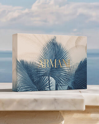 Un coffret cadeau Armani orne d'un motif botanique bleu, pose sur du marbre face a la mer. Un hommage a la collection "Armani Mare", melant savoir-faire couture et elegance solaire pour un rituel de beaute d'exception.