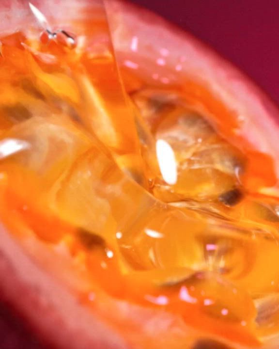 Un tres gros plan d'un maracuja (fruit de la passion) coupe, montrant les graines juteuses d'un orange vif et la pulpe avec de nombreux details. L'image a une texture chaude et brillante. En superposition, un texte blanc indique : « Une explosion acidulee et juteuse de Maracuja (Fruit de la passion) avec le delice sensuel et chaleureux de la Vanille ». En bas, se trouvent un lien « DECOUVRIR » et une icone de lecture blanche.