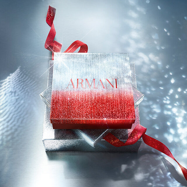 Boite cadeau Armani scintillante avec ruban rouge sur surface brillante.