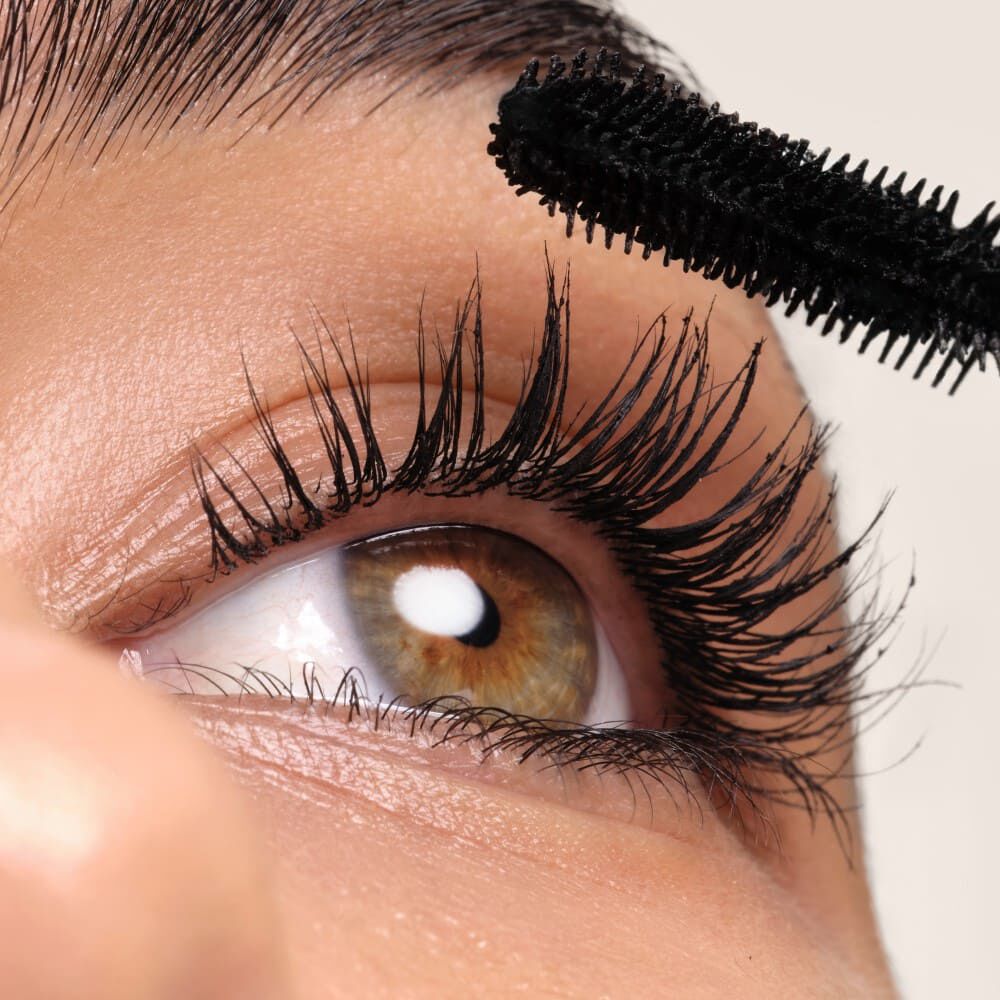 Une close-up d'un oeil mettant en avant des cils longs appliquant du mascara noir.