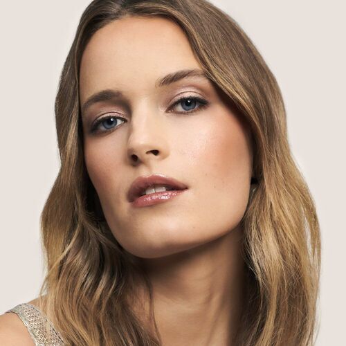A close-up portrait of a woman with long, wavy hair and a natural makeup look, featuring a soft expression and light background.