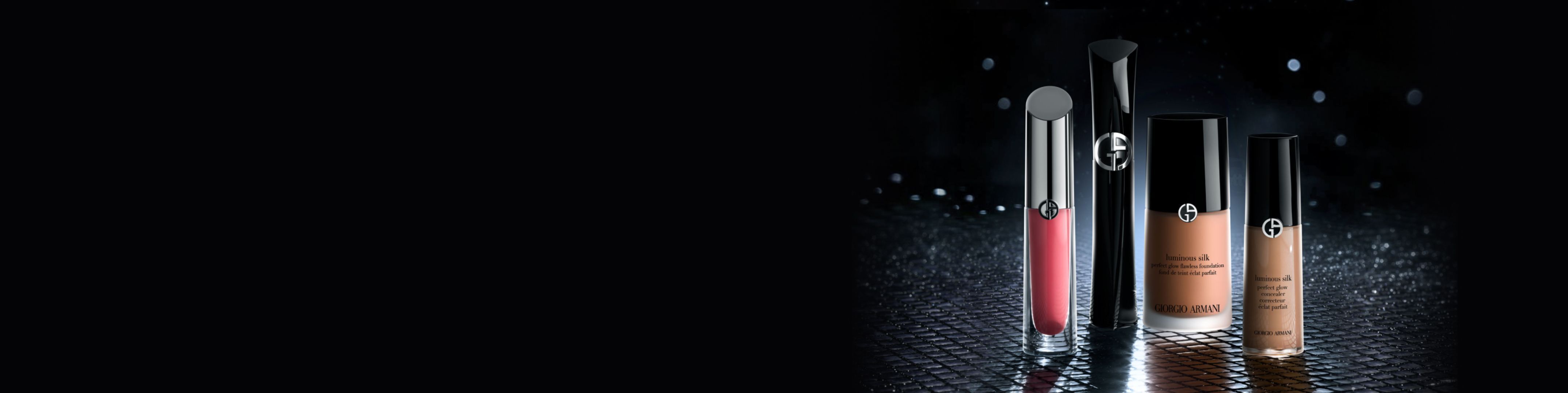 Armani Beauty make-up op donkere achtergrond: rode liplak, zwarte mascara, Luminous Silk foundation en concealer op een reflecterend oppervlak.