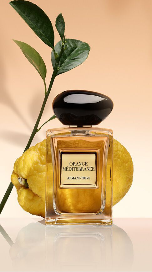 Armani/Prive Orange Mediterranee : un flacon au nectar dore, devant un agrume frais et des feuilles vertes, rayonnant la chaleur ensoleillee de la Mediterranee.
