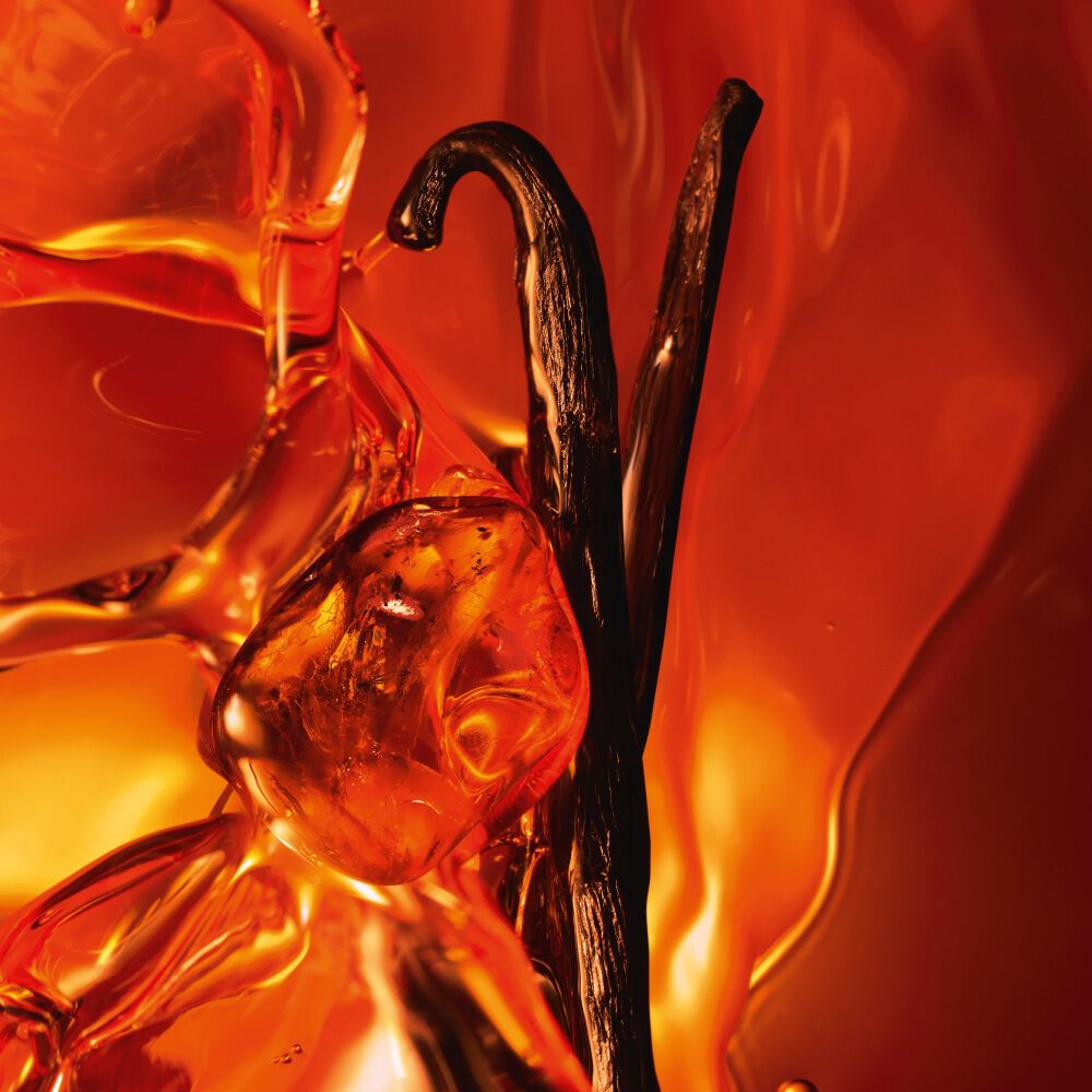 Een close-up van twee donkere vanillestokjes en glanzende amberhars tegen een warme, lichtgevende amberkleurige achtergrond.