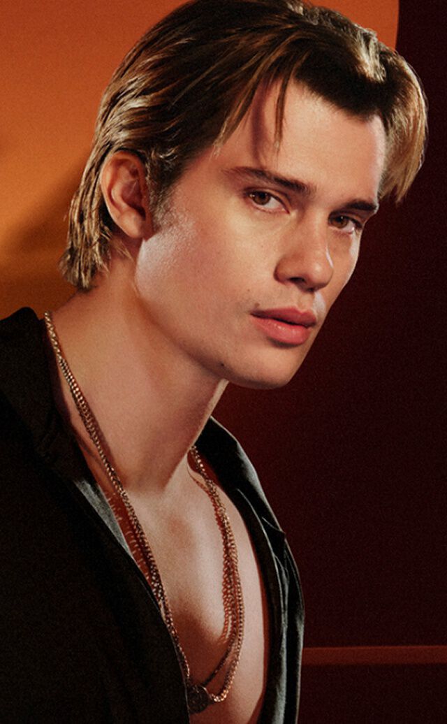 Une publicite pour la gamme de parfums « Stronger With You » d'Emporio Armani. A gauche, un jeune homme aux cheveux chatains porte une chemise noire et des colliers argentes, regardant l'objectif avec un regard serieux. A droite, un carrousel de produits sous le titre « EVERY FACET OF STRONGER WITH YOU » presente trois flacons de parfum differents. Le flacon central mis en evidence est « Stronger With You Powerfully » en format 50 ml, au prix de 74,00 £, avec un bouton « AJOUTER AU PANIER » en dessous. Des fleches de navigation et une barre de defilement sont egalement visibles.