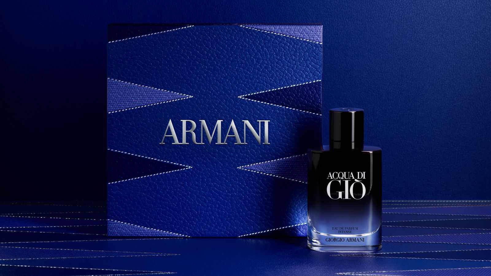 Flacon de parfum Giorgio Armani « Acqua di Gio » avec un coffret cadeau Armani bleu texture.