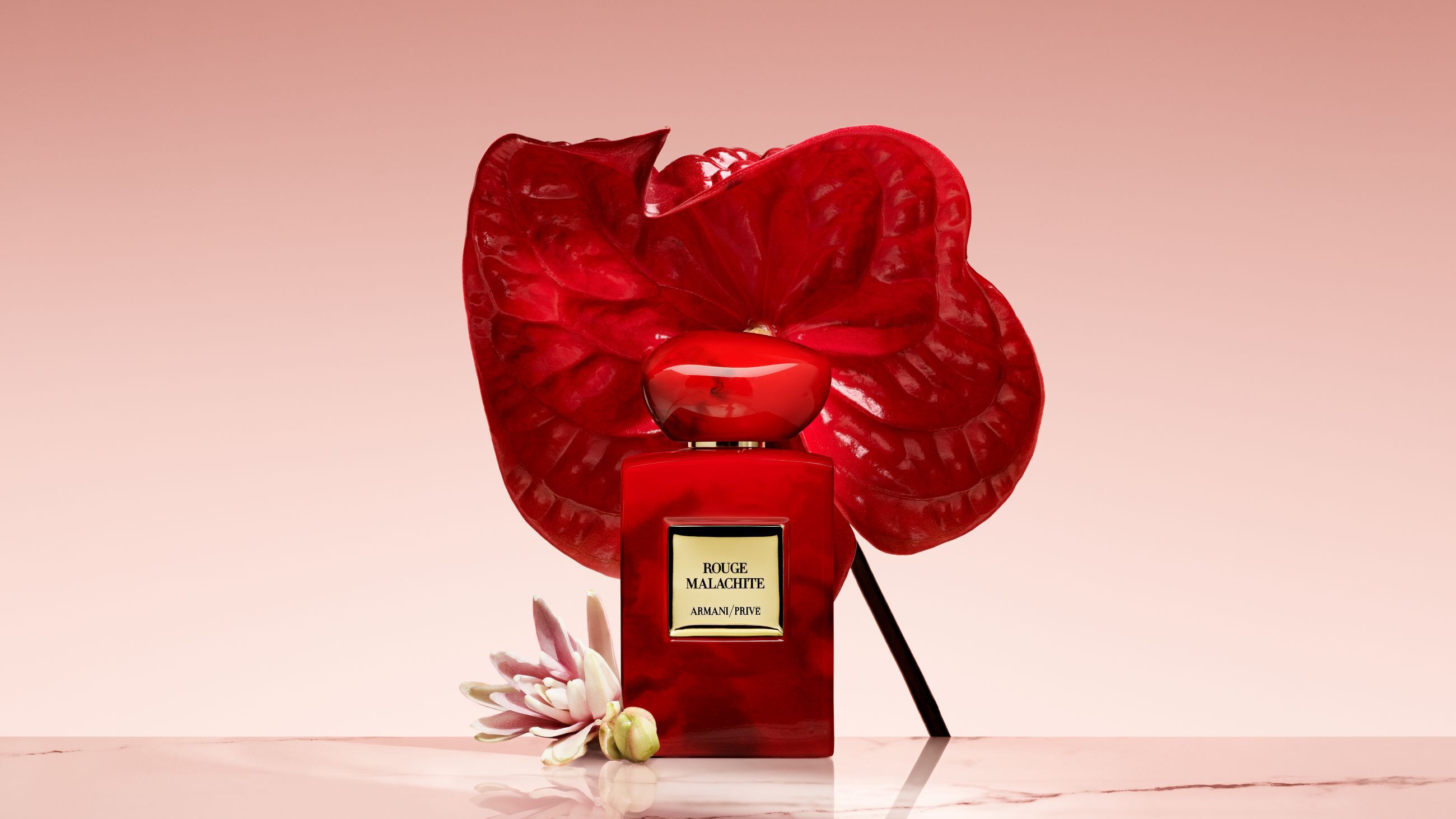 Flacon de parfum Armani/Prive Rouge Malachite devant une grande fleur rouge vif.
