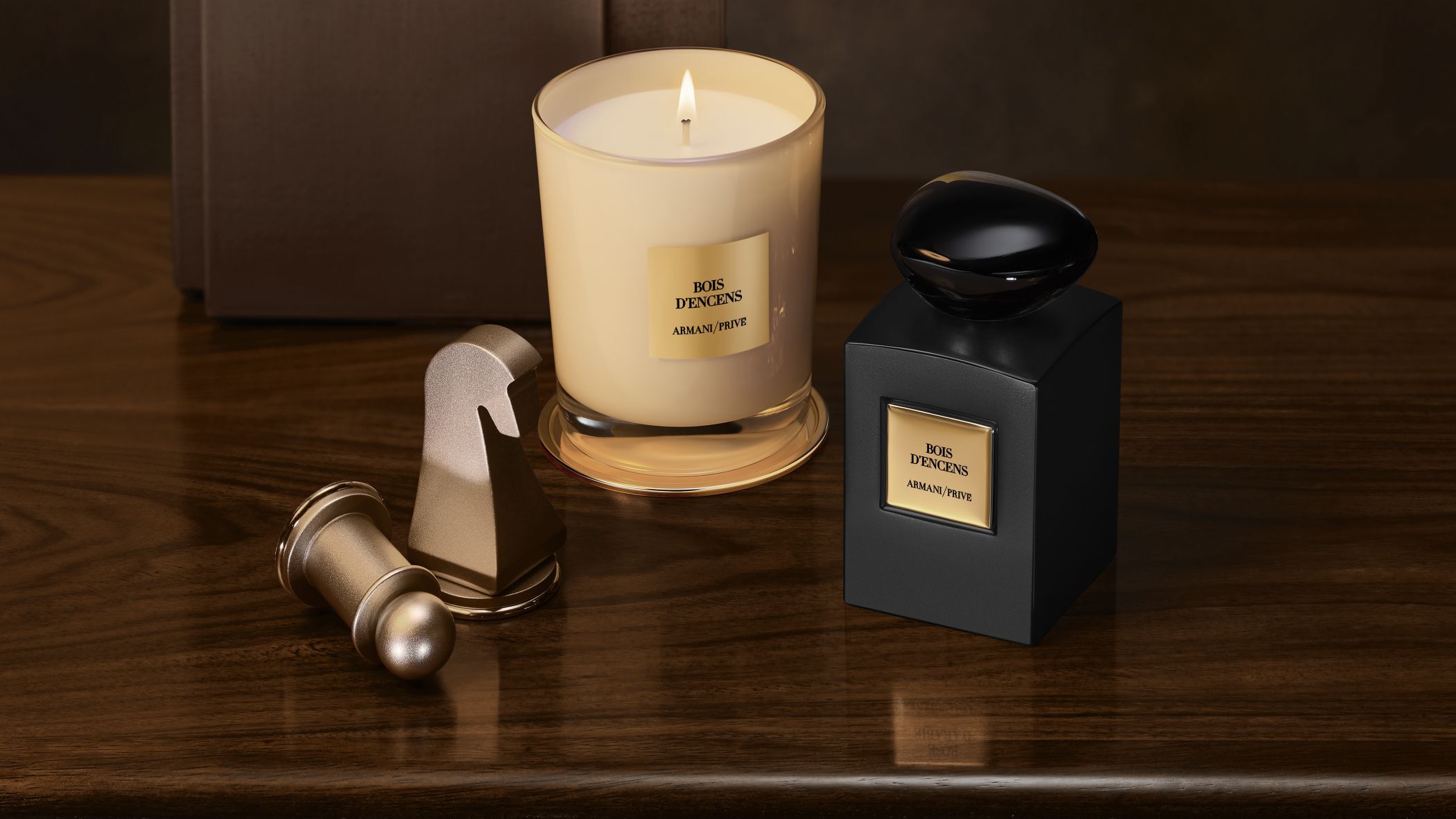 Flacon de parfum et bougie allumee Armani/Prive Bois d'Encens a cote de pieces d'echecs sur une table en bois.