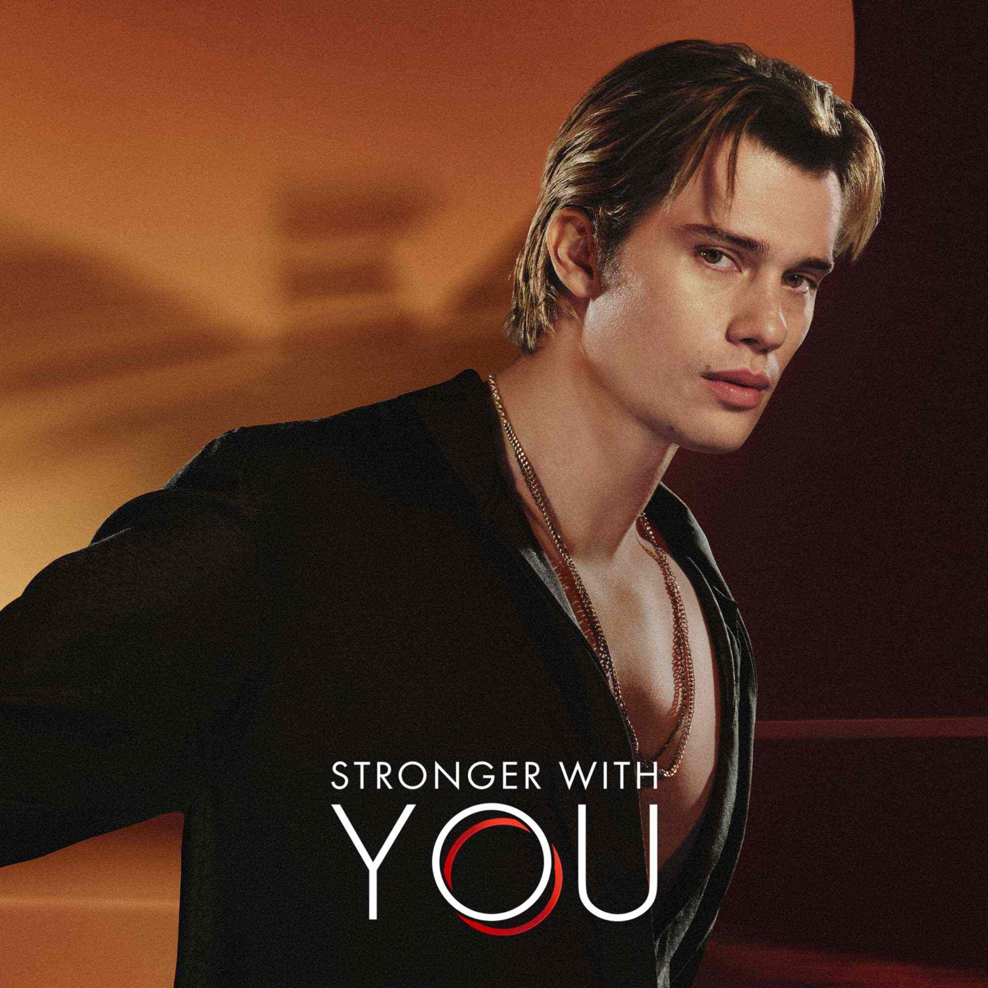 Nicholas Galatzine in een zwart shirt met de 'Stronger With You'-logotekst tegen een warme oranje achtergrond