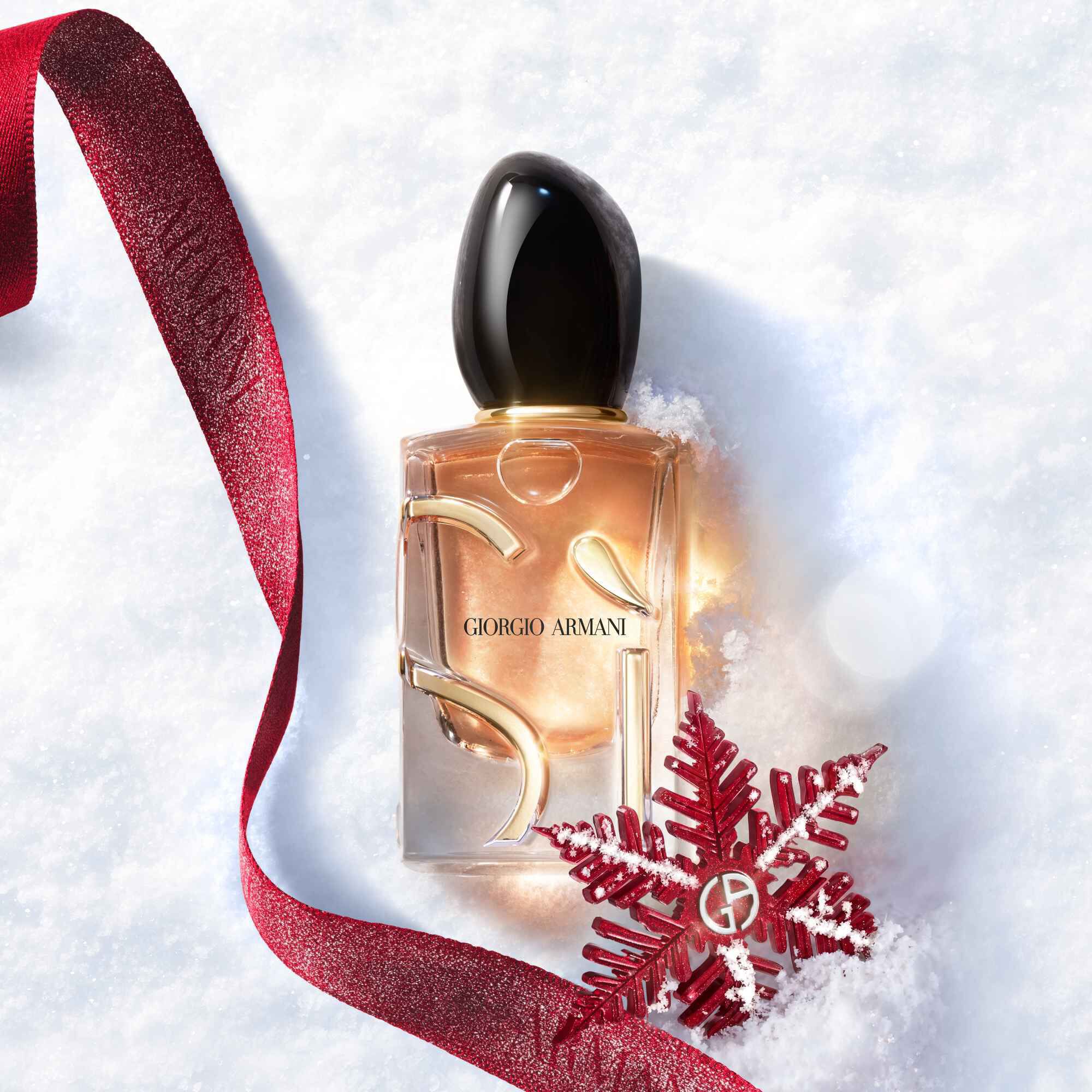 Si Eau de Parfum door Giorgio Armani, goudkleurige fles rustend in de sneeuw met een rood glitterlint en Giorgio Armani sneeuwvlokornament — een damesgeur, feestdagencadeau.