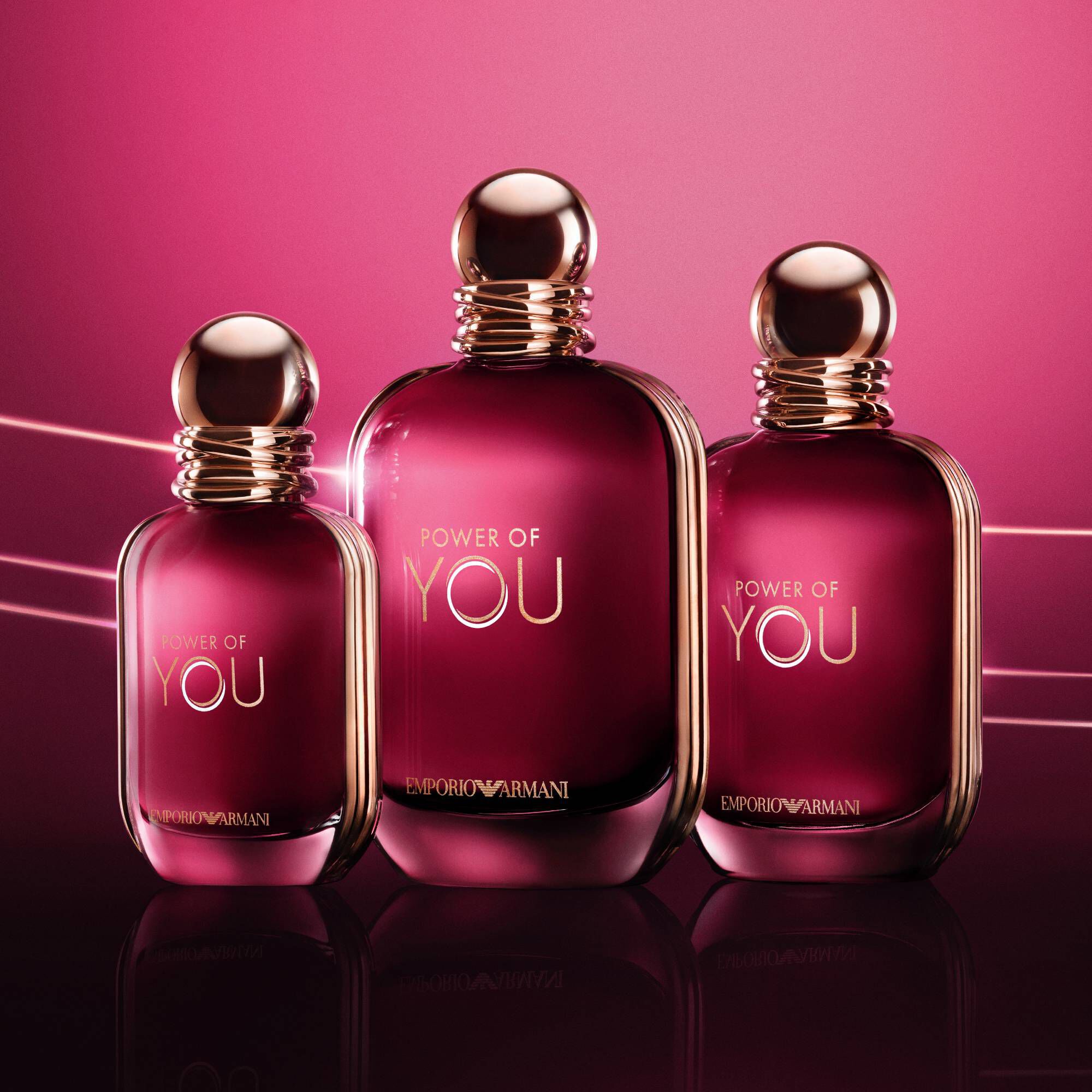 Drie ARMANI POWER OF YOU Eau de Parfum flessen — 30ml, 50ml en 100ml — die gloeien op een stralende robijnrode achtergrond.