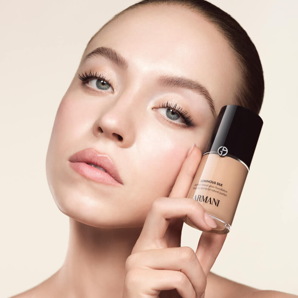 Sydney Sweeney holding a Giorgio Armani LUMINOUS SILK FOUNDATION bottle, emphasizing its natural radiance and silky texture