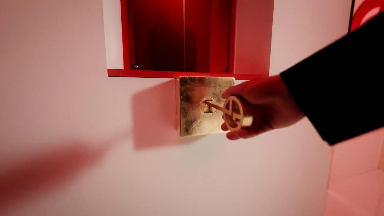 A hand holds a golden key, poised to unlock a red keyhole set against a white wall.