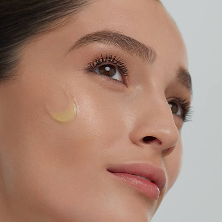 Une femme applique un sérum sur son visage, montrant une peau lumineuse et soignée.