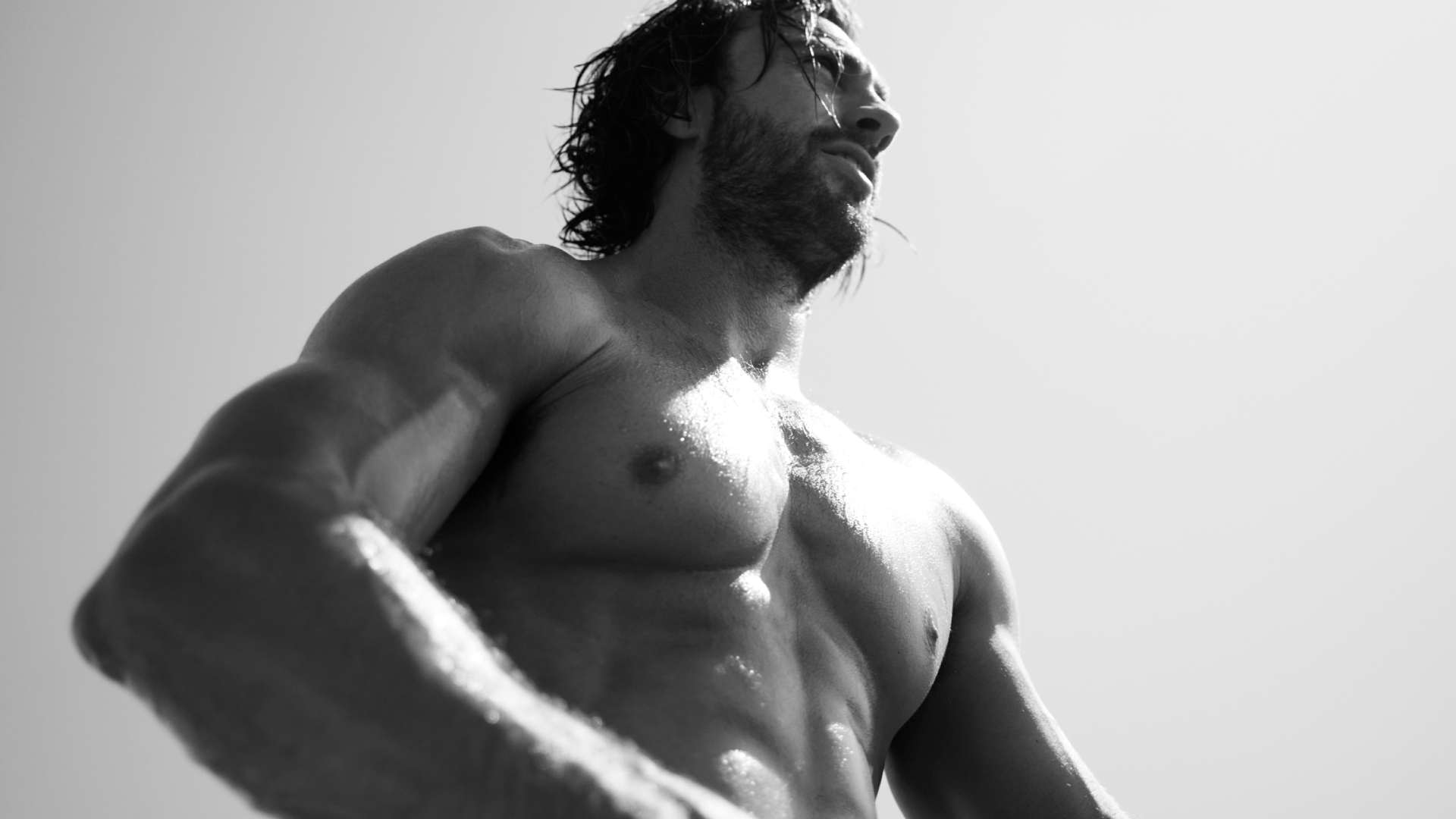 Un homme musclé, torse nu, se tient sous un soleil éclatant, capturant l'attention par sa posture dynamique.