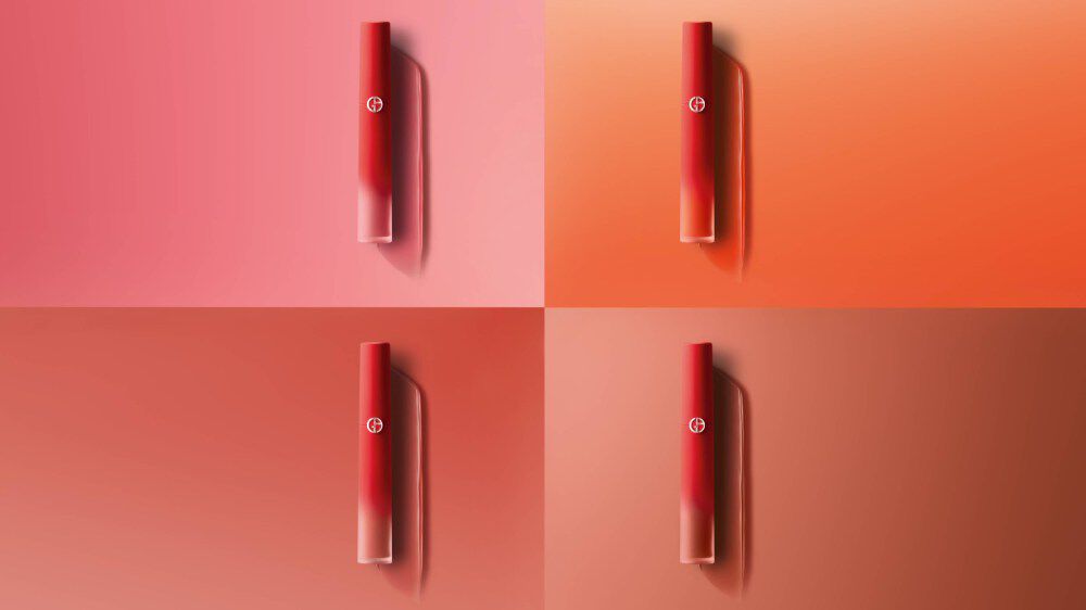 Quatre rouges à lèvres Giorgio Armani sur un fond dégradé dans des teintes rose et orange.
