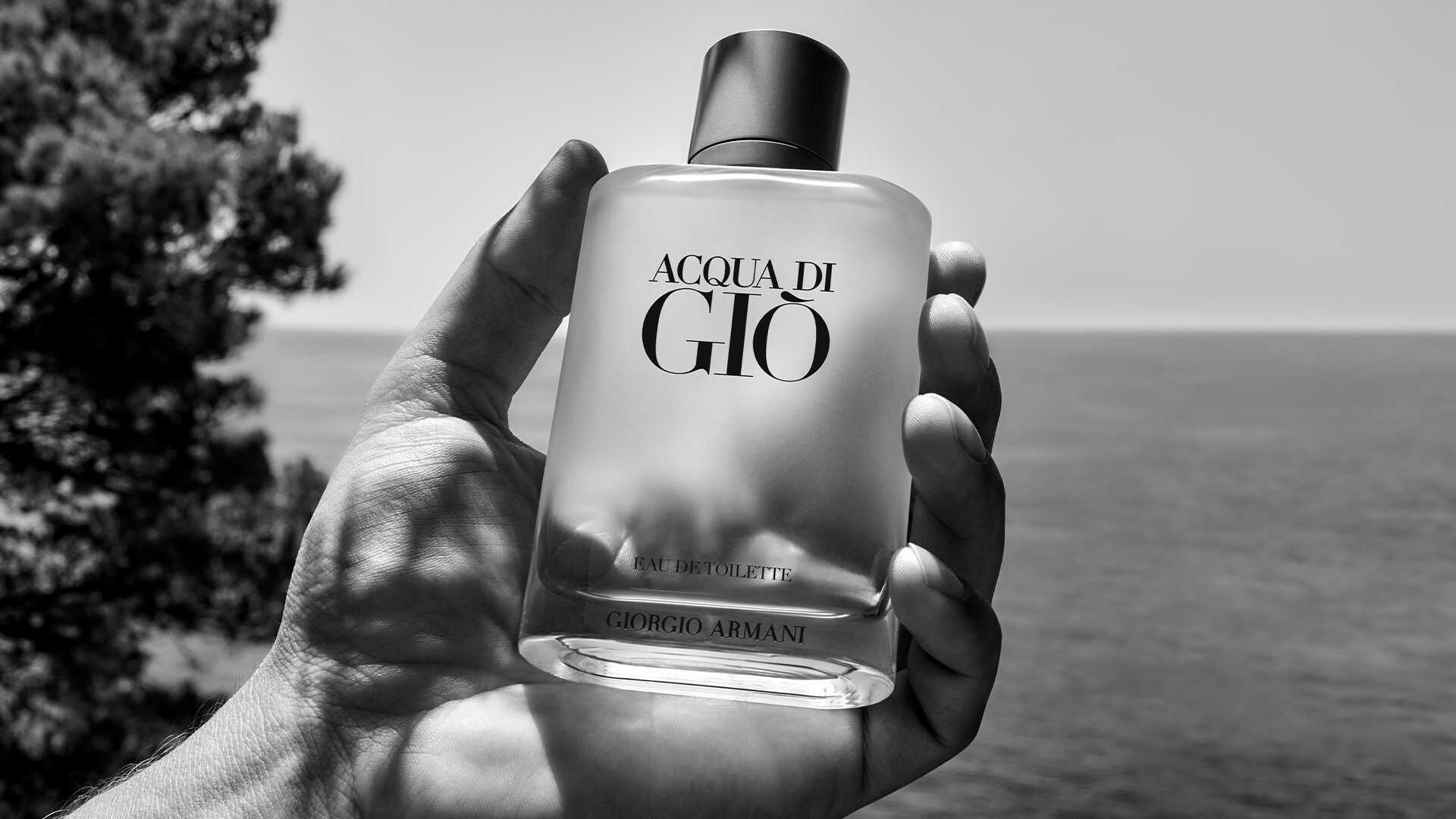 Un homme tient un flacon de parfum Acqua di Giò de Giorgio Armani devant la mer.
